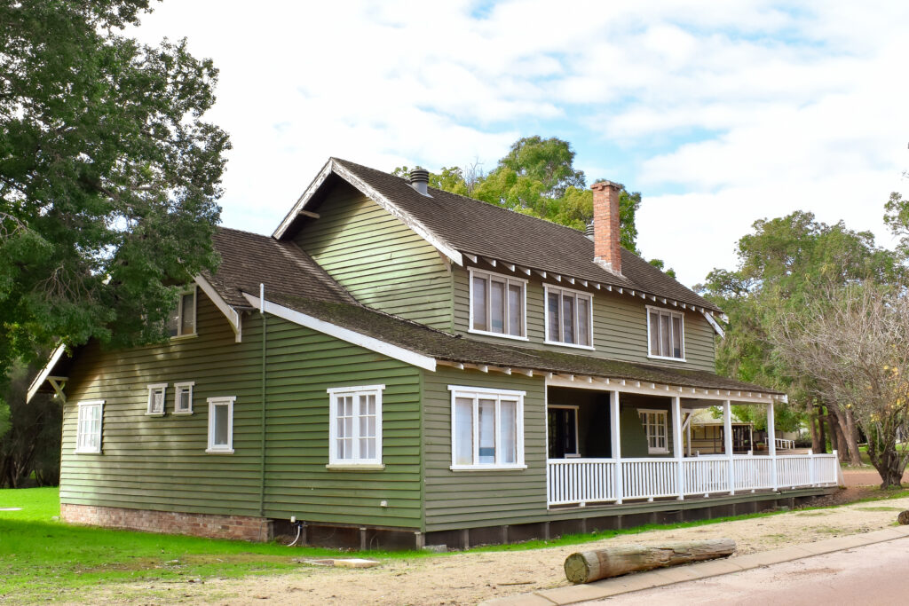 Green Belfast Cottage, complemented by a tree in front, located in the southwest accommodation area of Fairbridge Village