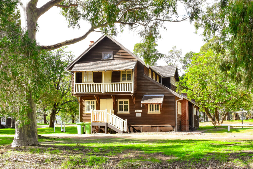 Exterior view of Fairbridge Village Evelyn Cottage in brown, surrounded by tall and green leafy trees