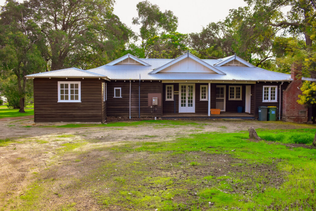 Front view of a cosy brown Nightingale Cottage, surrounded by tall trees; a southwest accommodation at Fairbridge Village