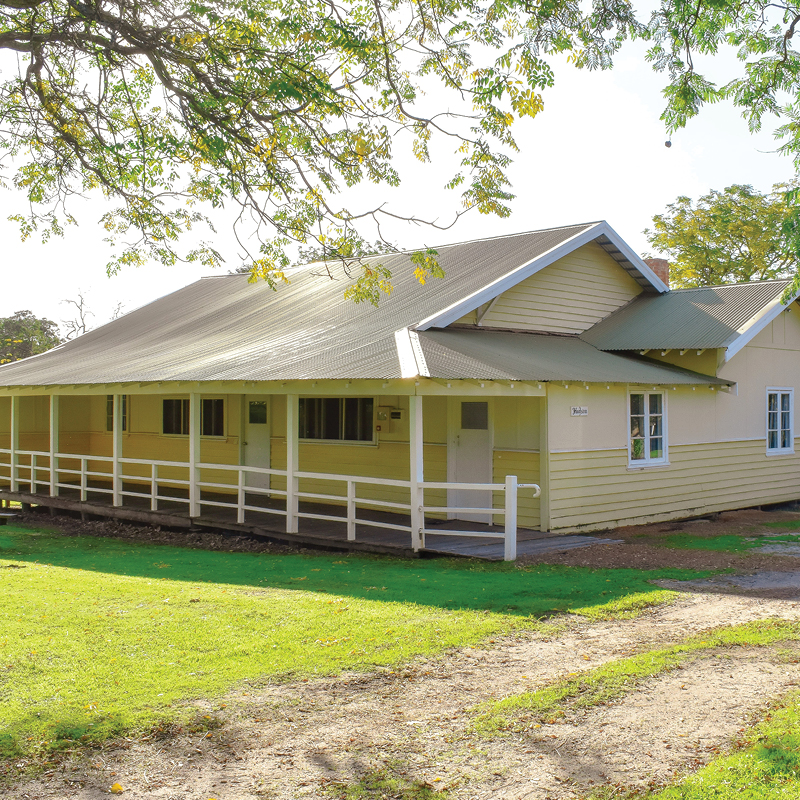 A yellow Hudson Cottage surrounded by trees, a southwest accommodation in Fairbridge Village