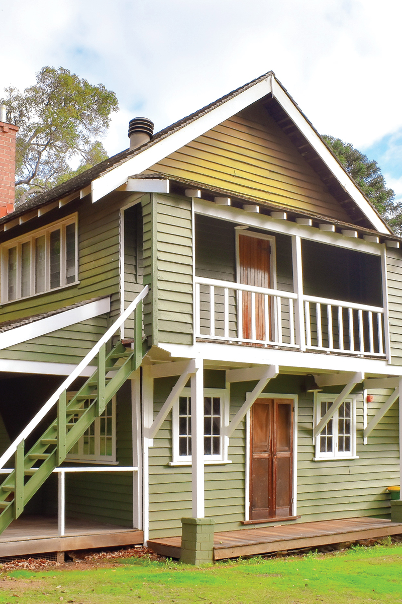 Side view of large green Middlemore Cottage with a porch and balcony nestled at Fairbridge Village