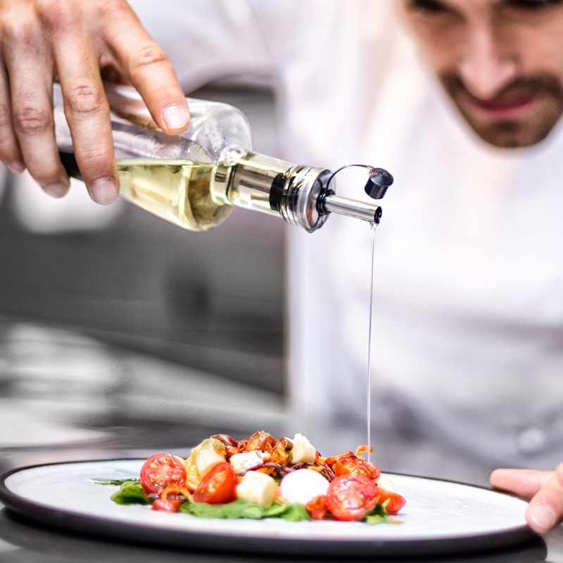 A chef skillfully pours olive oil onto a plate at Fairbridge Village dining