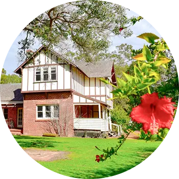A charming house surrounded by a garden with vibrant red flowers and tall trees, located in southwest accommodation area