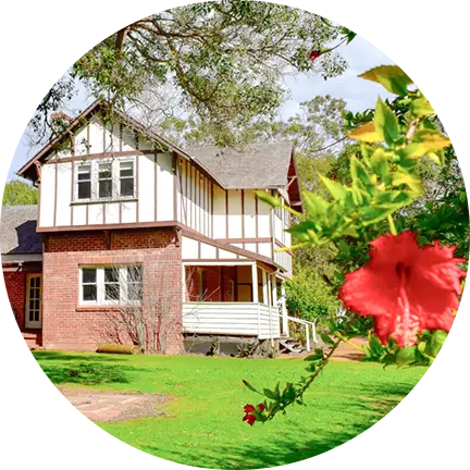 A charming house surrounded by a garden with vibrant red flowers and tall trees, located in southwest accommodation area