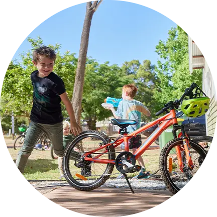 Two kids are running and playing with water guns beside a parked bicycle, surrounded by vibrant trees at Fairbridge Village