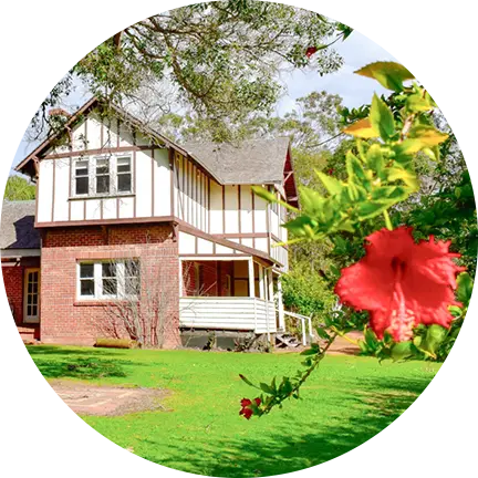 A charming house surrounded by a garden with vibrant red flowers and tall trees, located in southwest accommodation area