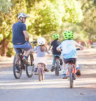 Three kids enjoy cycling with their mentor on a dirt road surrounded by green leafy trees