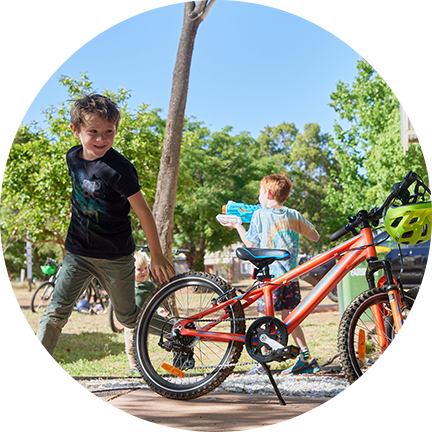 Two kids are running and playing with water guns beside a parked bicycle, surrounded by vibrant trees at Fairbridge Village