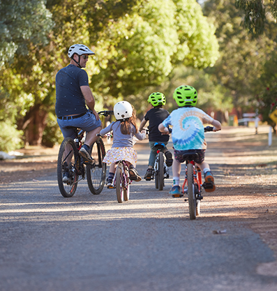 Three kids enjoy cycling with their mentor on a dirt road surrounded by green leafy trees